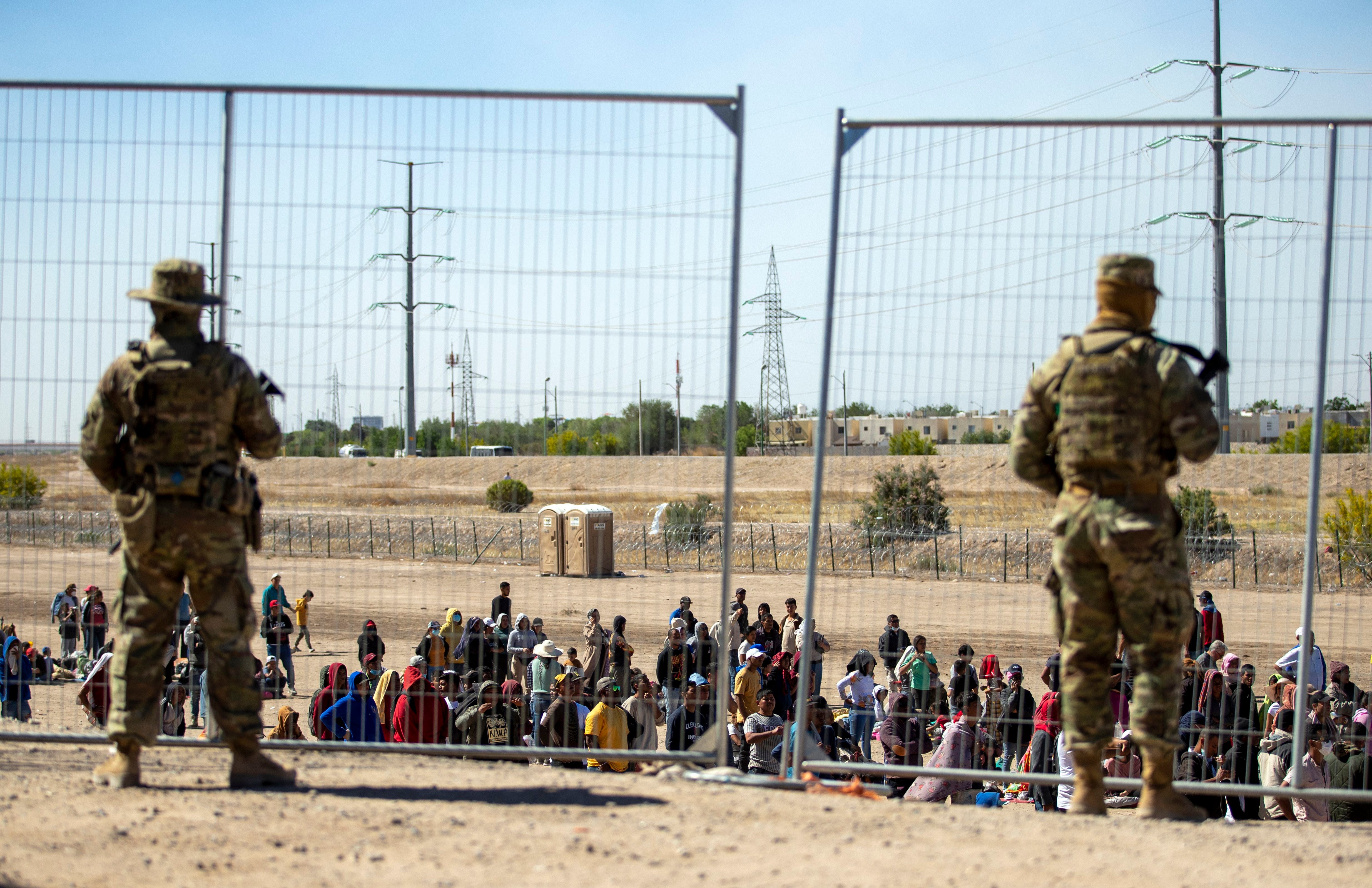 Migrantes esperan junto a una valla fronteriza bajo la vigilancia de la Guardia Nacional para ingresar a El Paso, Texas (AP Foto/Andres Leighton/Archivo)