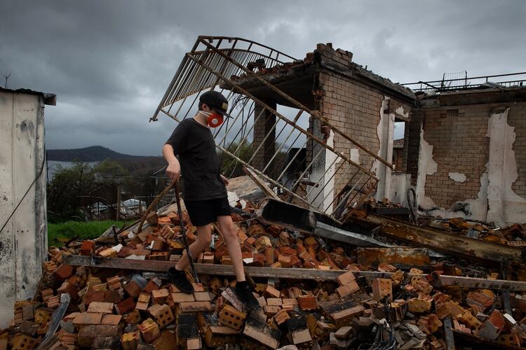 Riley Fletcher, 12, walks on the ruins of his family’s home in Conjola Park, Australia on Feb. 16, 2020. He is wearing a mask to protect himself from asbestos. Devastating floods came soon after the bush fires in Australia as scientists call it “compound extremes,” as one climate disaster intensifying the next. (Matthew Abbott/The New York Times)