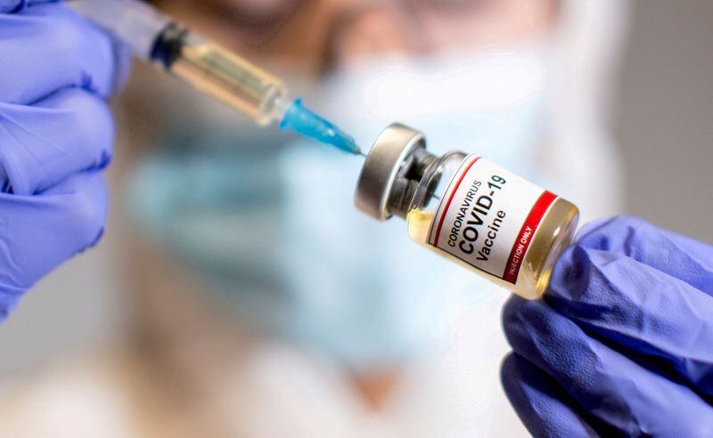 FILE PHOTO: A woman holds a small bottle labelled with a "Coronavirus COVID-19 Vaccine" sticker and a medical syringe in this illustration taken  October 30, 2020. REUTERS/Dado Ruvic/File Photo