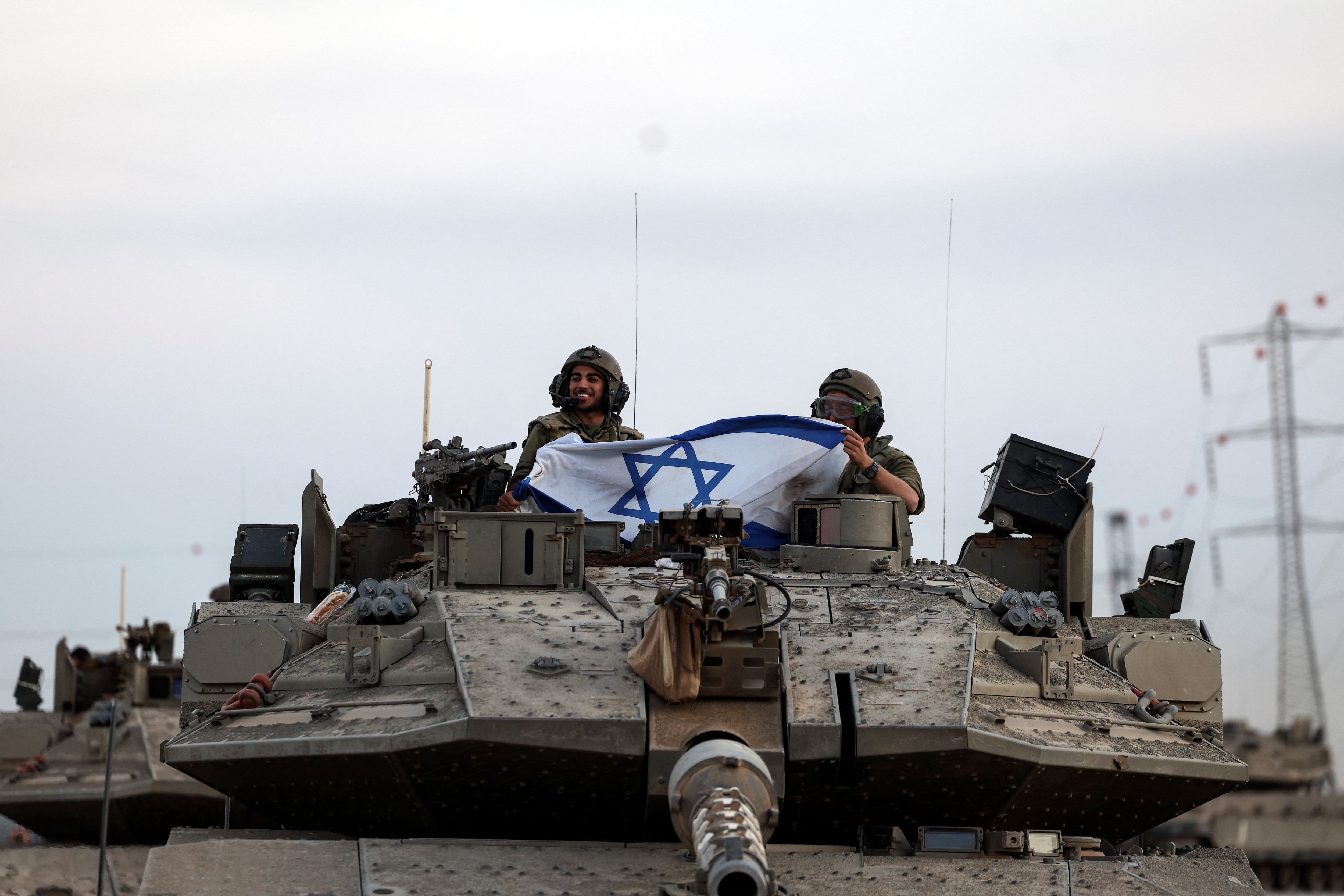 Soldados israelíes sostienen una bandera israelí en un tanque cerca de la frontera de Israel con la Franja de Gaza, en el sur de Israel, 12 de octubre de 2023 (Reuters-Ronen Zvulun)