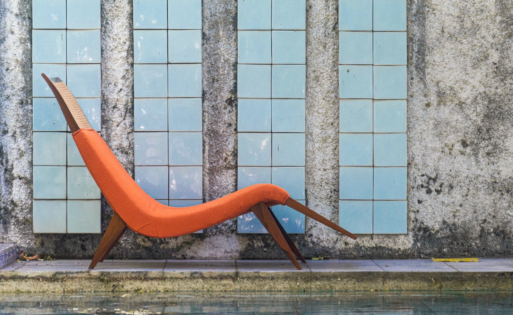 Una chaise longue en madera y textil naranja junto a una pared y un curso de agua en Design Miami 2022