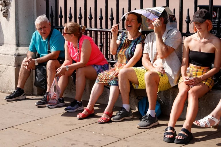 Las personas se refugian del sol debajo de un mapa durante el clima cálido, en las afueras del Palacio de Buckingham en  
