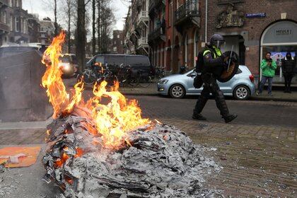 Un policía camina cerca de una hoguera durante una protesta contra las restricciones en Ámsterdam (REUTERS/Eva Plevier)