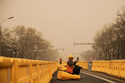 Un trabajador de la carretera usa su teléfono inteligente en Beijing, China, mientras la ciudad está envuelta en bruma después de una tormenta de arena. REUTERS/Thomas Peter