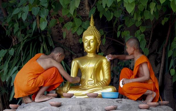 Dos monjes limpian una escultura de Buda durante una ceremonia religiosa para celebrar el Día de Buda en Tailandia (EFE)