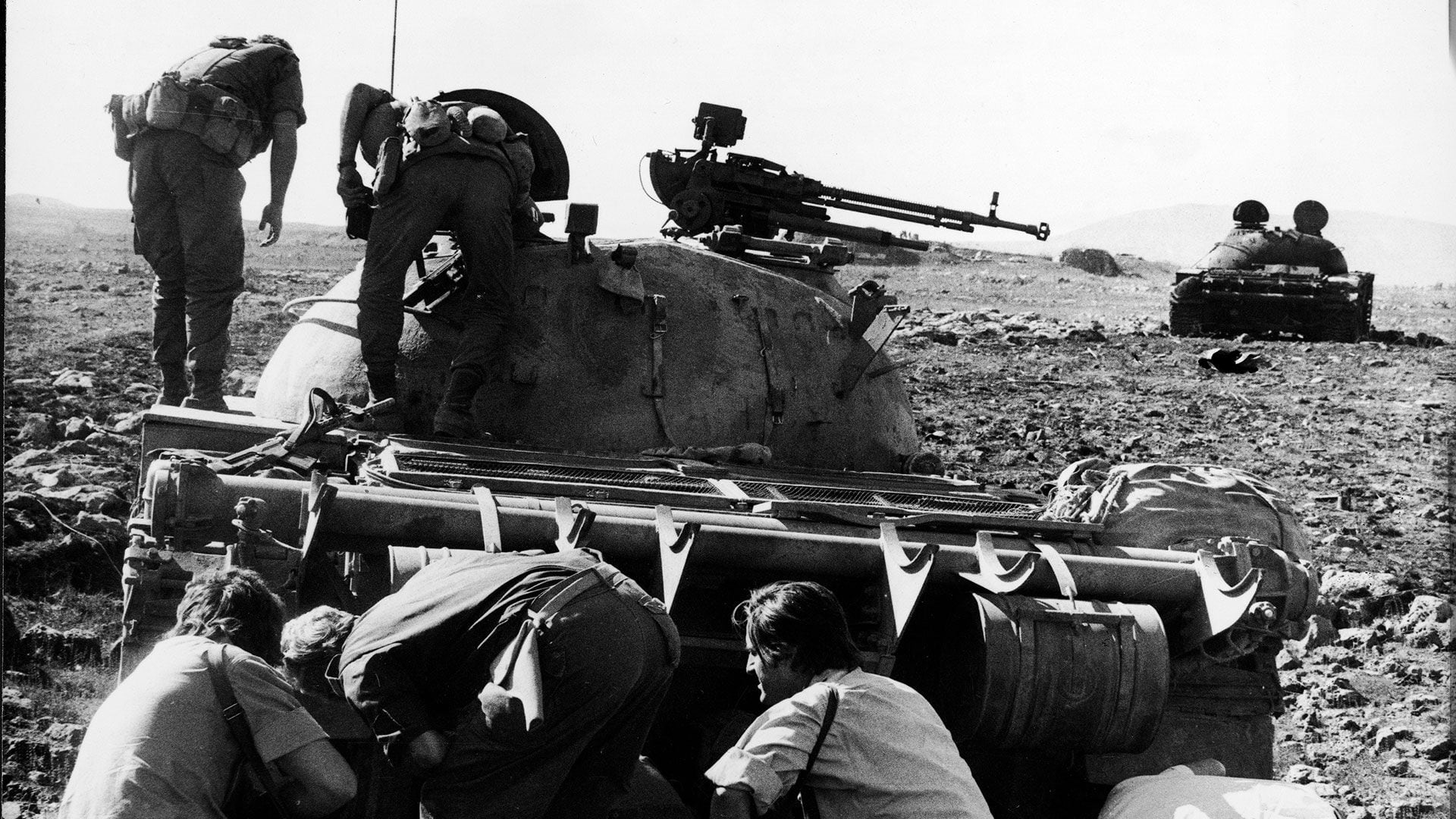 Un conductor de tanque sirio herido escondido bajo su tanque T-62 de fabricación soviética destruido por los israelíes durante la Guerra del Yom Kippur, octubre de 1973. Dos sodliers israelíes inspeccionan la torreta del vehículo. (Foto de Hulton Archive/Getty Images)