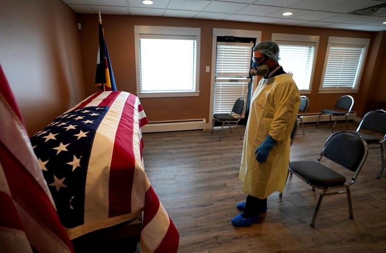 Michael Neel, director funerario de All Veterans Funeral and Cremation, con el equipo completo de protección personal, mira la bandera estadounidense en el ataúd de George Trefren, un veterano de la Guerra de Corea de 90 años que murió de la enfermedad coronavirus (COVID-19) en un asilo, en Denver, Colorado, EE.UU. el 23 de abril de 2020. (REUTERS)