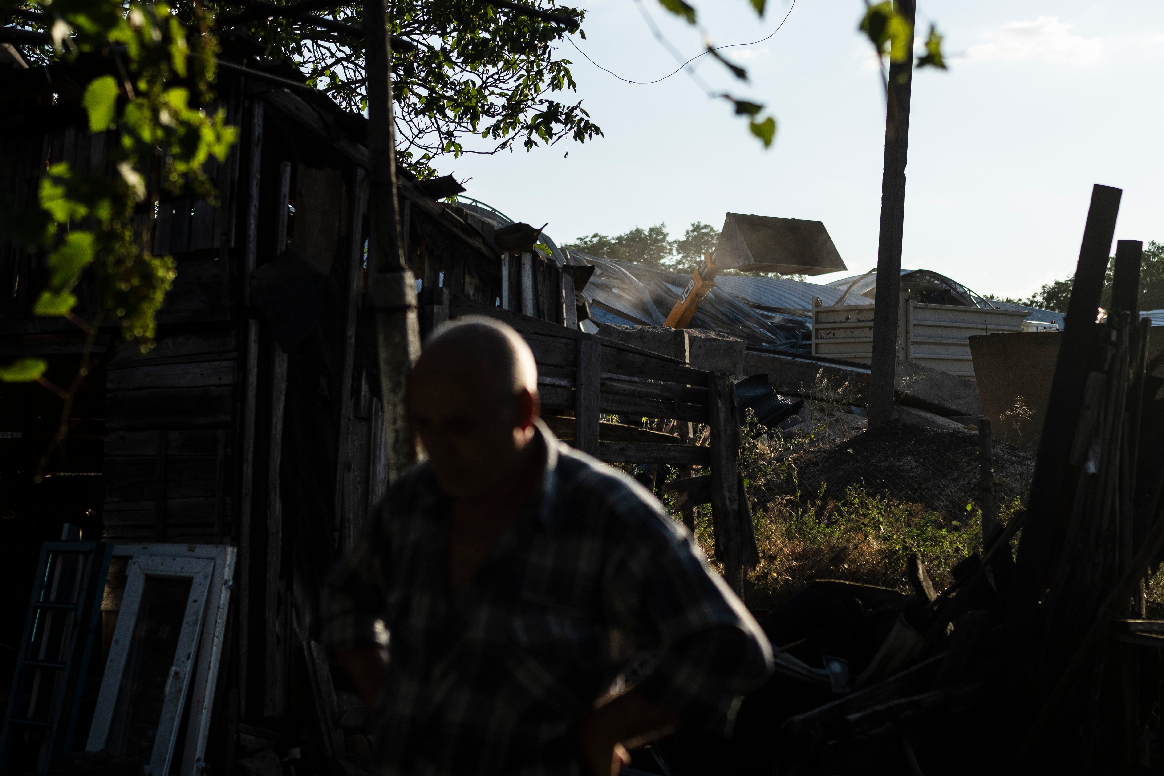 Un residente, cuya casa ha resultado gravemente dañada por los ataques con misiles rusos contra una fábrica de grano situada junto a su casa, se detiene un momento mientras un cargador vierte el grano recuperable en un camión de transporte. (AP Foto/Jae C. Hong)