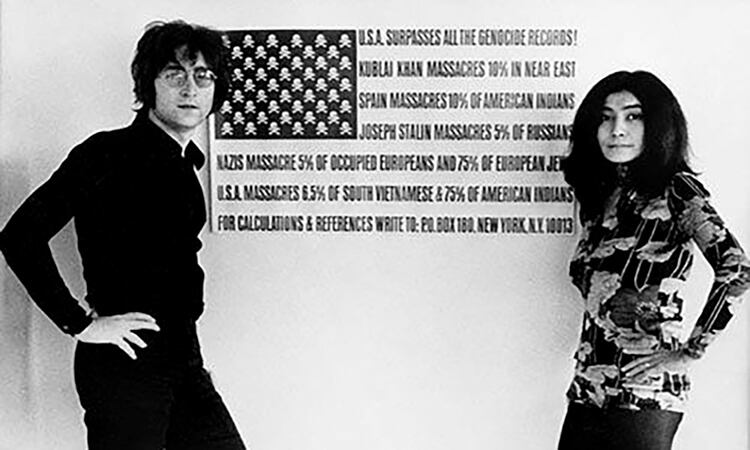 John Lennon posa al lado de un dibujo que simula la bandera de los Estados Unidos mencionando el resultado de las guerras en el mundo. 