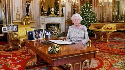 La reina Isabel II brinda su tradicional mensaje navideño desde el Palacio Buckingham en 2018. En su escritorio se puede ver una fotografía de los duques de Cambridge y de los Sussex junto al príncipe Carlos. En el fondo aparece otra fotografía del casamiento de Harry y Meghan Markle 