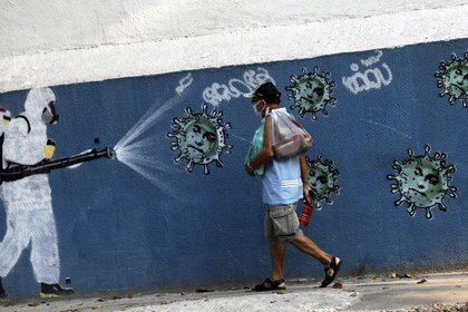 Un hombre camina junto a un grafiti que muestra a un limpiador con equipo de protección rociando virus con la cara del presidente de Brasil Jair Bolsonaro, en medio del brote de la enfermedad coronavirus (COVID-19), en Río de Janeiro, Brasil. 7 de octubre de 2020. REUTERS/Ricardo Moraes