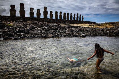 Niños juegan en el océano detrás de Ahu Tongariki, en la Isla de Pascua (Josh Haner/The New York Times)