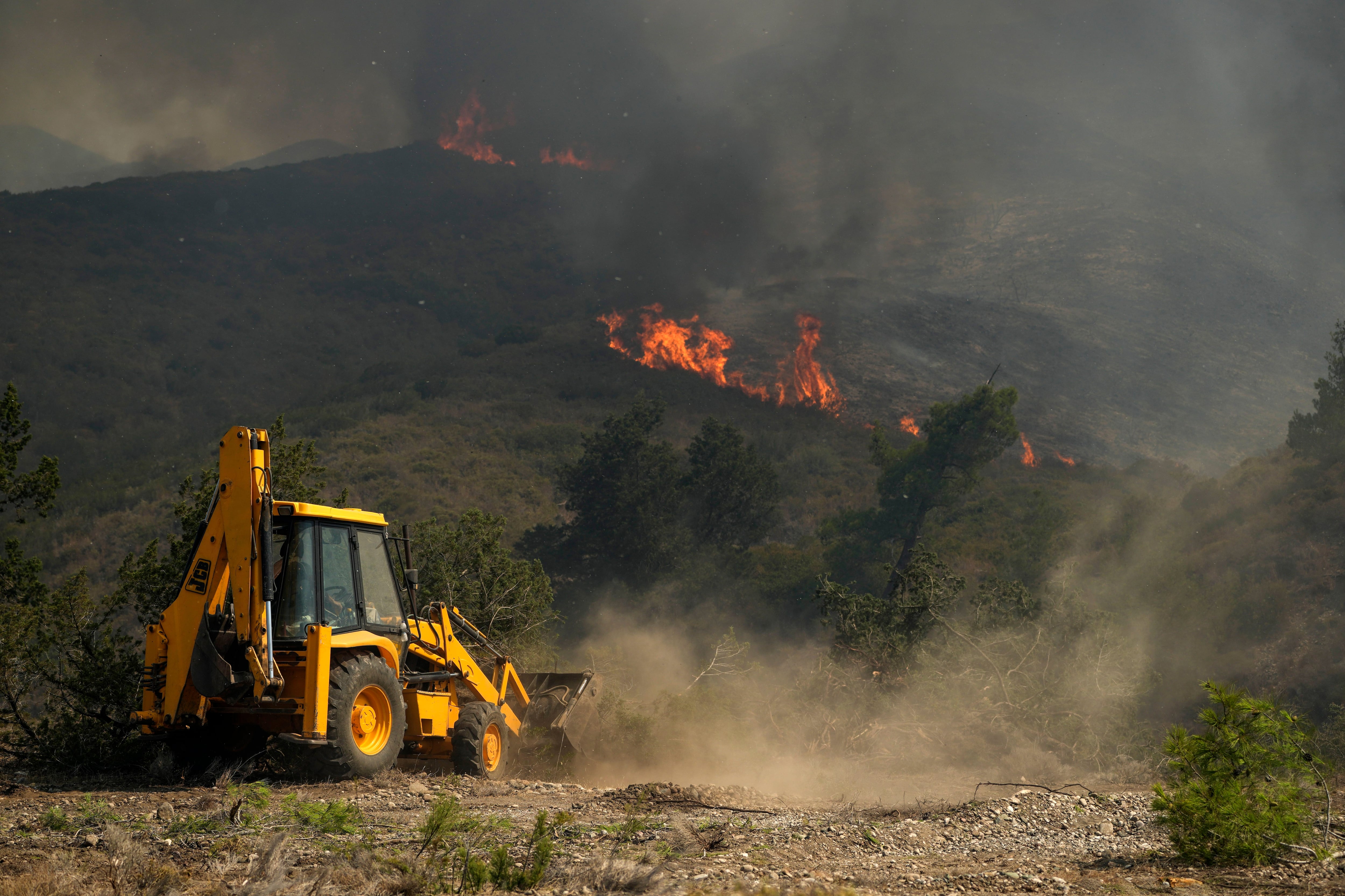 Una excavadora abre un cortafuegos durante un incendio forestal en la aldea de Vati, en la isla de Rodas, en el mar Egeo, en el sureste de Grecia, el martes 25 de julio de 2023. (Foto AP/Petros Giannakouris)