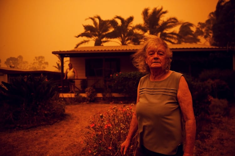 Nancy Allen y Brian Allen se detienen afuera de su casa mientras los fuertes vientos empujan humo y cenizas del Currowan Fire hacia Nowra, New South Wales, Australia, el 4 de enero de 2020. El cielo naranja tiñe toda la geografía del país (Reuters)