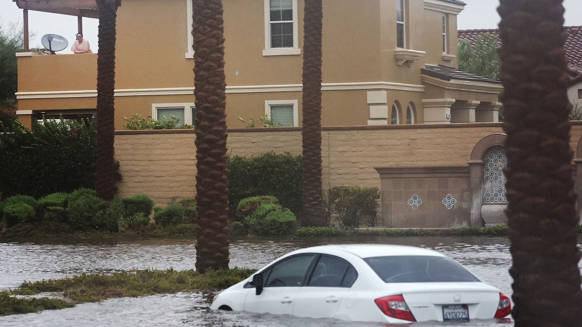Una persona mira desde una residencia hacia un automóvil parcialmente sumergido en las aguas de la inundación mientras la tormenta tropical Hilary avanza por el área en Cathedral City, California.