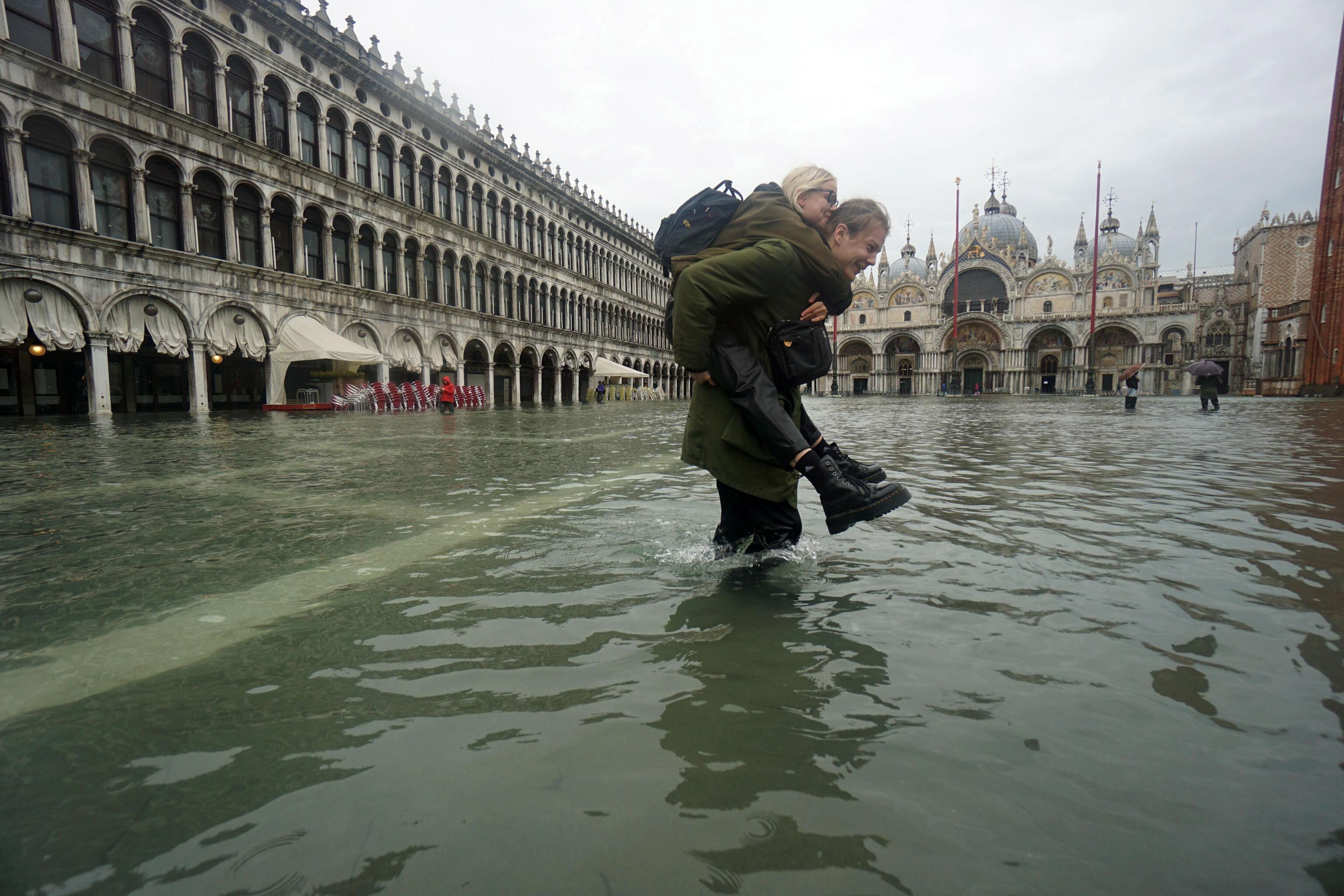 Un hombre lleva a una mujer a través de las aguas de la inundación en la Plaza de San Marcos (EFE/EPA/ANDREA MEROLA)