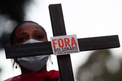 Una mujer sostiene una cruz con un mensaje mientras asiste a un homenaje por las casi 100.000 muertes del COVID-19 y una protesta contra el presidente brasileño Jair Bolsonaro en Sao Paulo, Brasil.  7 de agosto de 2020. REUTERS / Amanda Perobelli