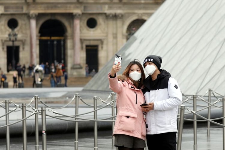 Una pareja que usa máscaras posa para un autorretrato cerca de la Pirámica del Louvre en París, Francia. 5 de marzo, 2020. REUTERS/Charles Platiau