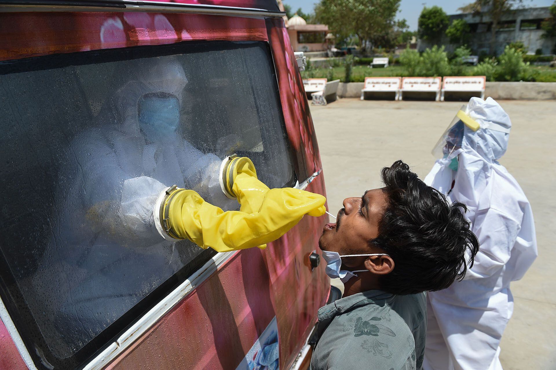 Un funcionario de salud utiliza un hisopo para recoger una muestra de un hombre para la prueba de COVID-19 desde el interior de una furgoneta móvil en la aldea de Changodar, a unos 20 kms de Ahmedabad, el 23 de abril de 2020. (Foto de SAM PANTHAKY / AFP)