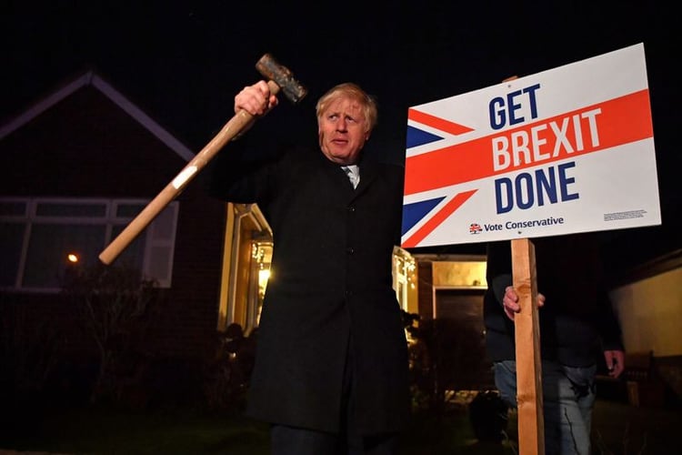 El primer ministro británico, Boris Johnson, luce victorioso luego de clavar un letrero con la consigna 