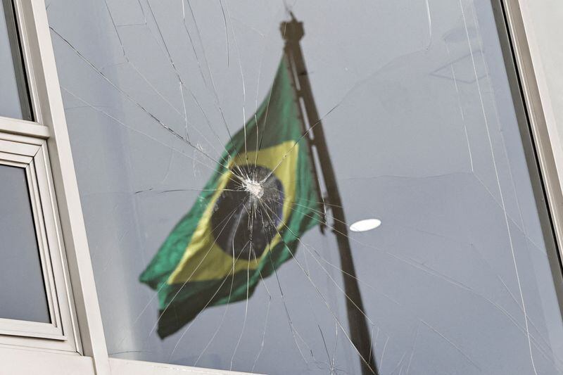 La bandera de Brasil se refleja en una ventana rota, después de que los partidarios del ex presidente Jair Bolsonaro participaran en un disturbio antidemocrático en el Palacio de Planalto, en Brasilia (REUTERS/Ueslei Marcelino/Archivo)