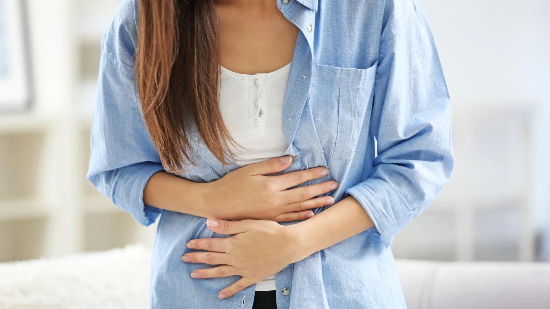 Young woman suffering from abdominal pain at home, closeup. Gynecology concept