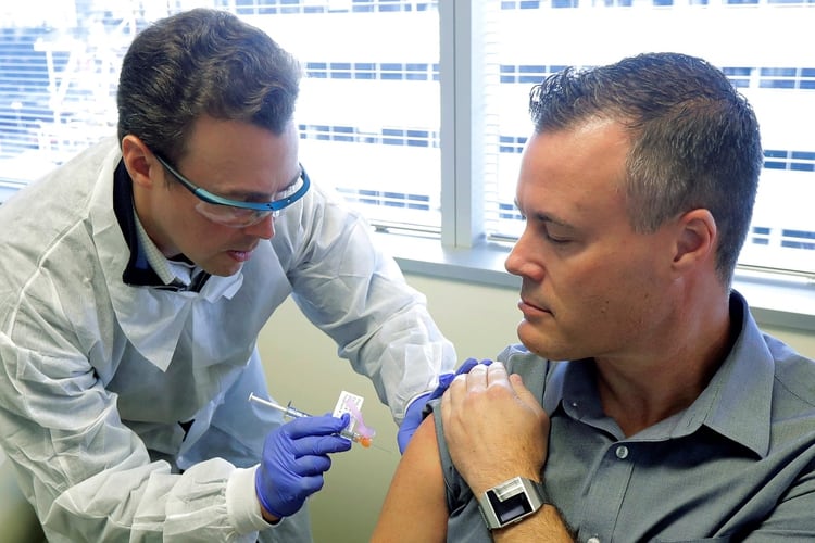El farmacéutico Michael Witte le suministra a Neal Browning (derecha) una inyección en el ensayo clínico de la primera etapa del estudio de seguridad de una posible vacuna para COVID-19 (AP)