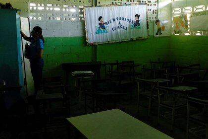 Una maestra junto a una valla publicitaria que dice "Bienvenidos a las clases" y pupitres vacíos en un aula el primer día de clases, en Caucagua, Venezuela Septiembre 17, 2018. REUTERS/Marco Bello