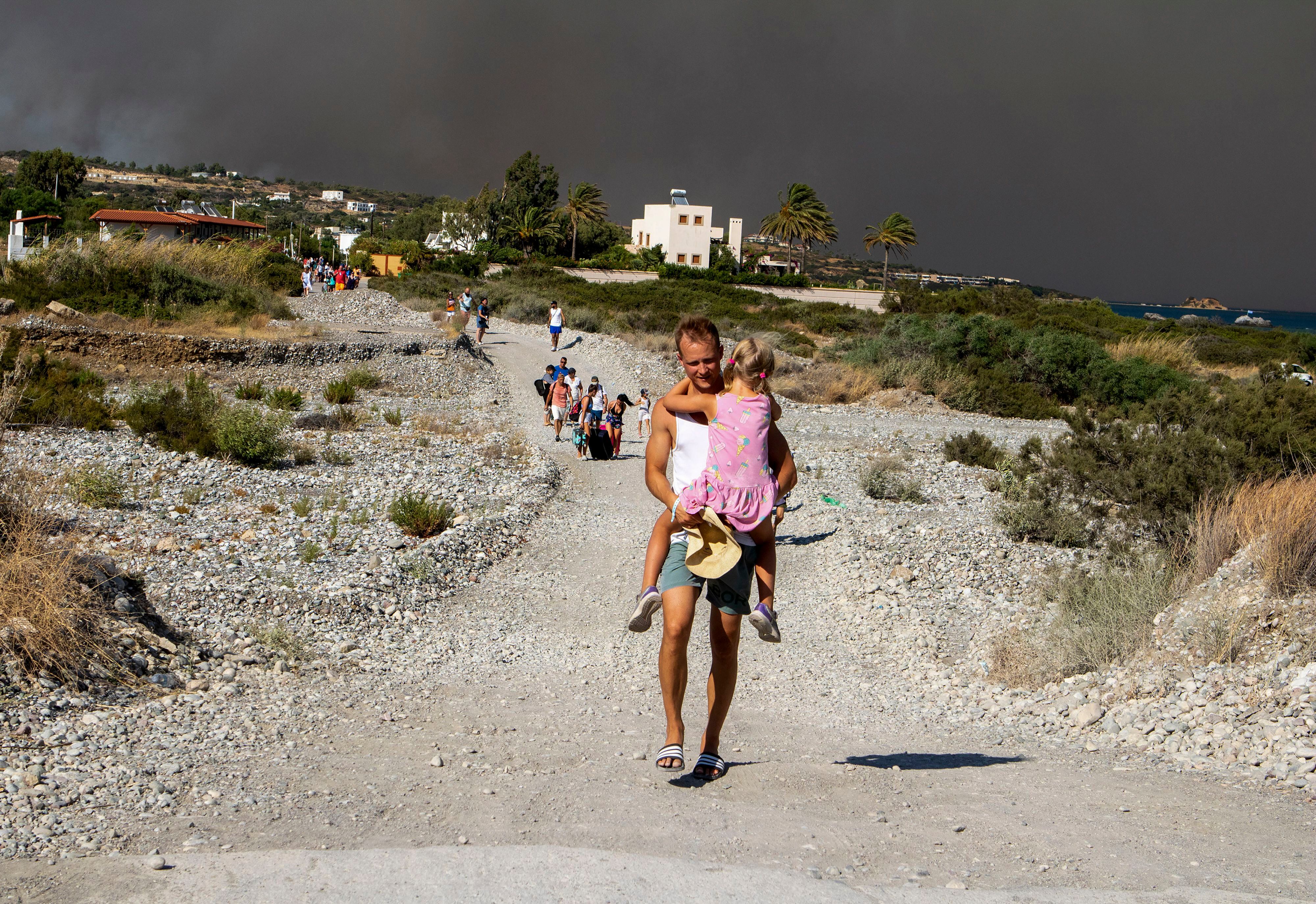 Un hombres lleva a una niña al abandonar la zona donde arde un incendio forestal en la isla de Rodas (Lefteris Diamanidis/InTime News via AP)