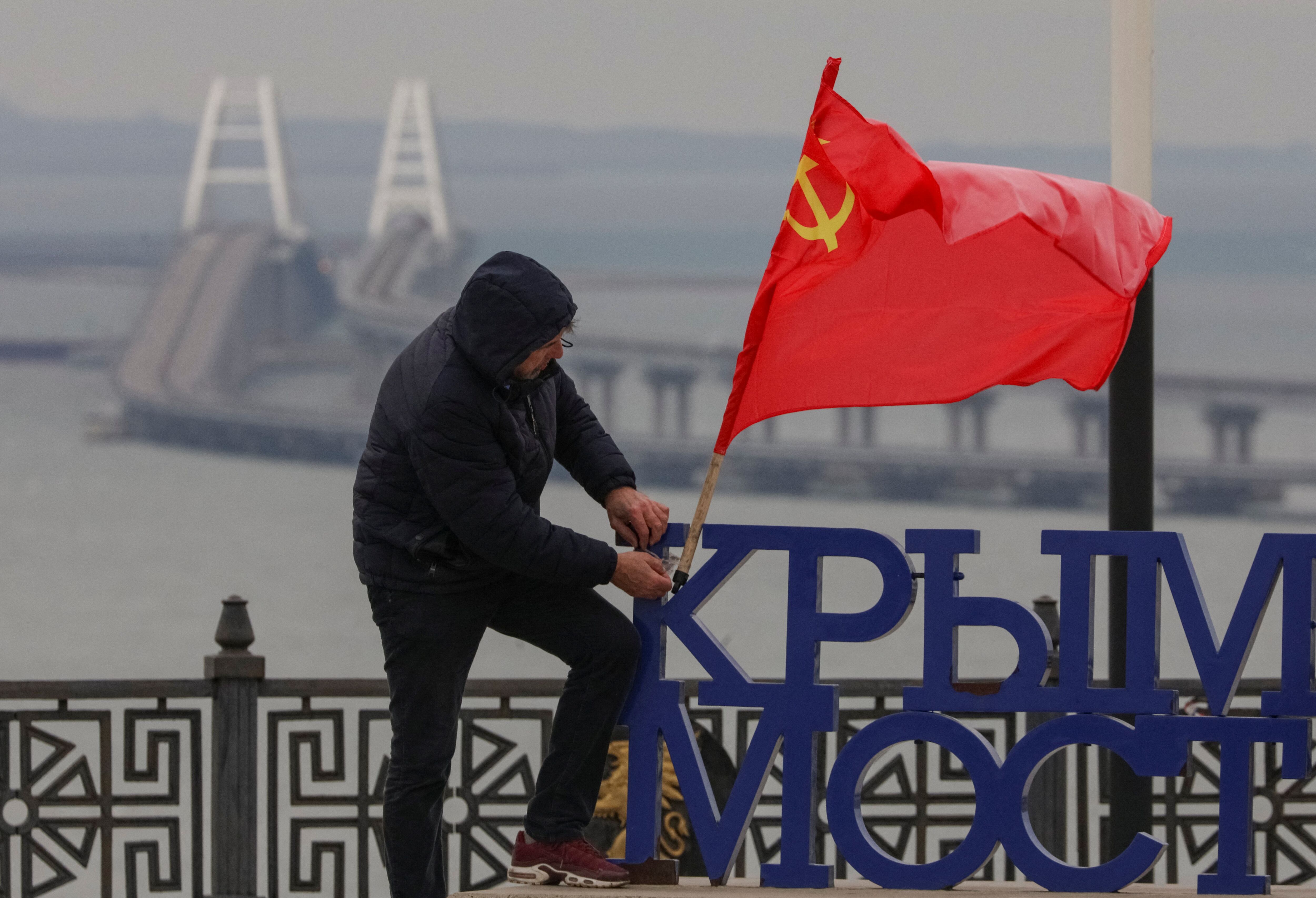 Un hombre pone una bandera soviética en un punto de observación, con el telón de fondo del puente de Crimea en el estrecho de Kerch. REUTERS/Alexey Pavlishak