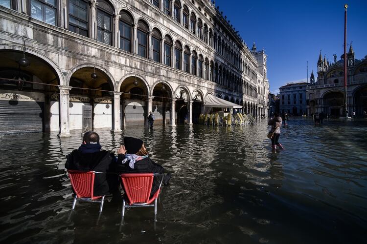 Dos personas sentadas en sillas de bistro en medio de la inundada Plaza San Marcos el 14 de noviembre de 2019 en Venecia. (AFP)