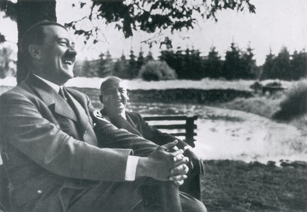 Sentado en un banco al aire libre, el dictador alemán nacido en Austria, Adolf Hitler (1889-1945), se ríe a carcajadas con un hombre no identificado cerca de la cordillera de Harz, Alemania, 1935. (Getty)