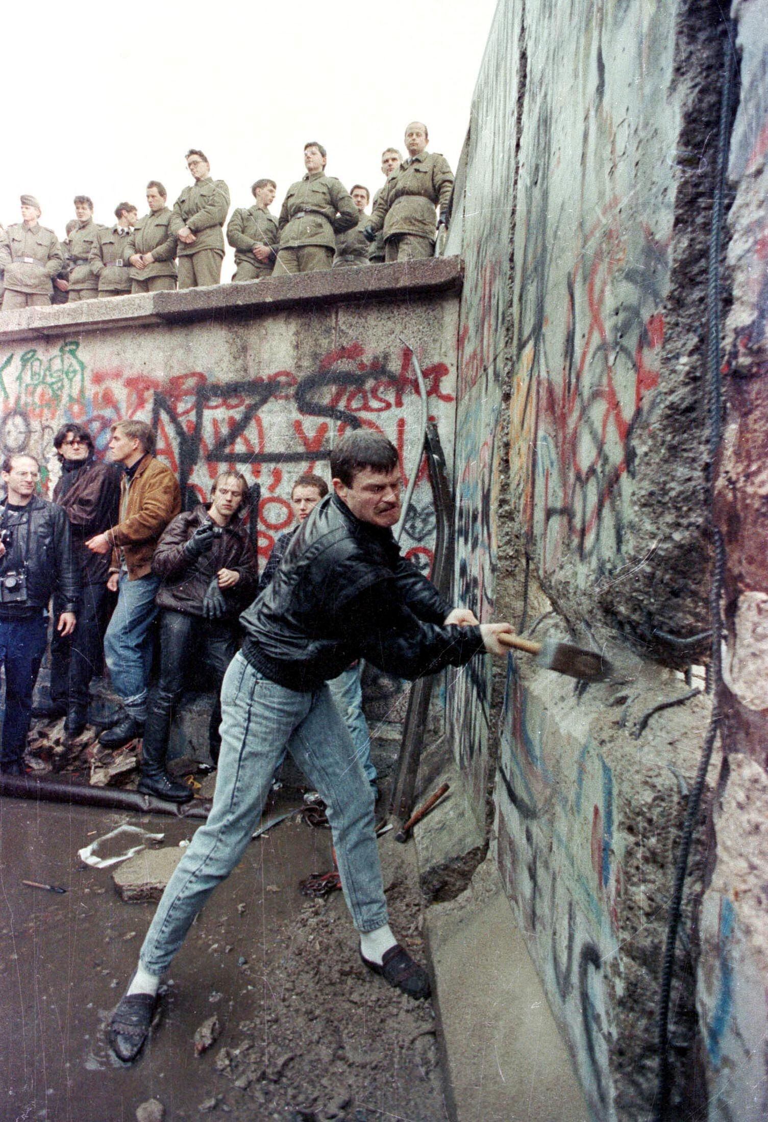 FOTO DE ARCHIVO: Un manifestante golpea el Muro de Berlín mientras los guardias fronterizos de Berlín Oriental miran desde arriba de la Puerta de Brandenburgo en esta foto de archivo del 11 de noviembre de 1989. 