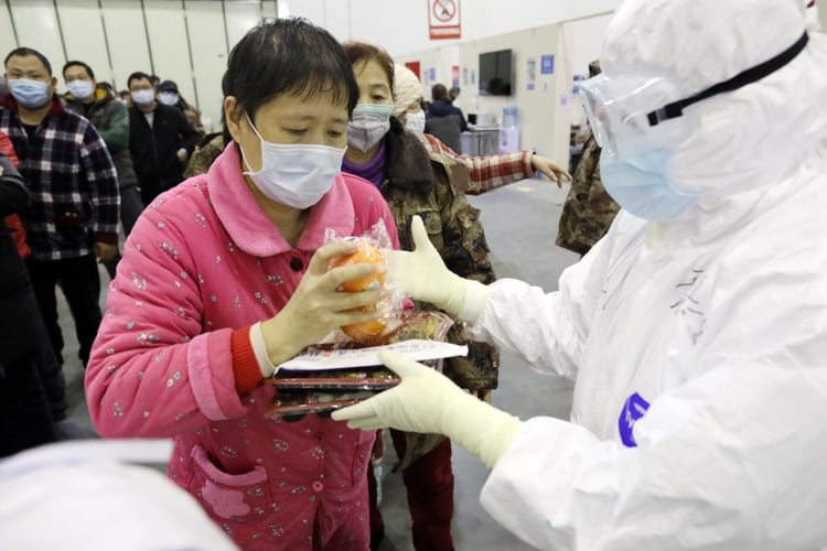 Una paciente recibe su almuerzo de un trabajador médico en el Centro de Convenciones de Wuhan Parlor que se ha convertido en un hospital improvisado (China Daily via REUTERS)