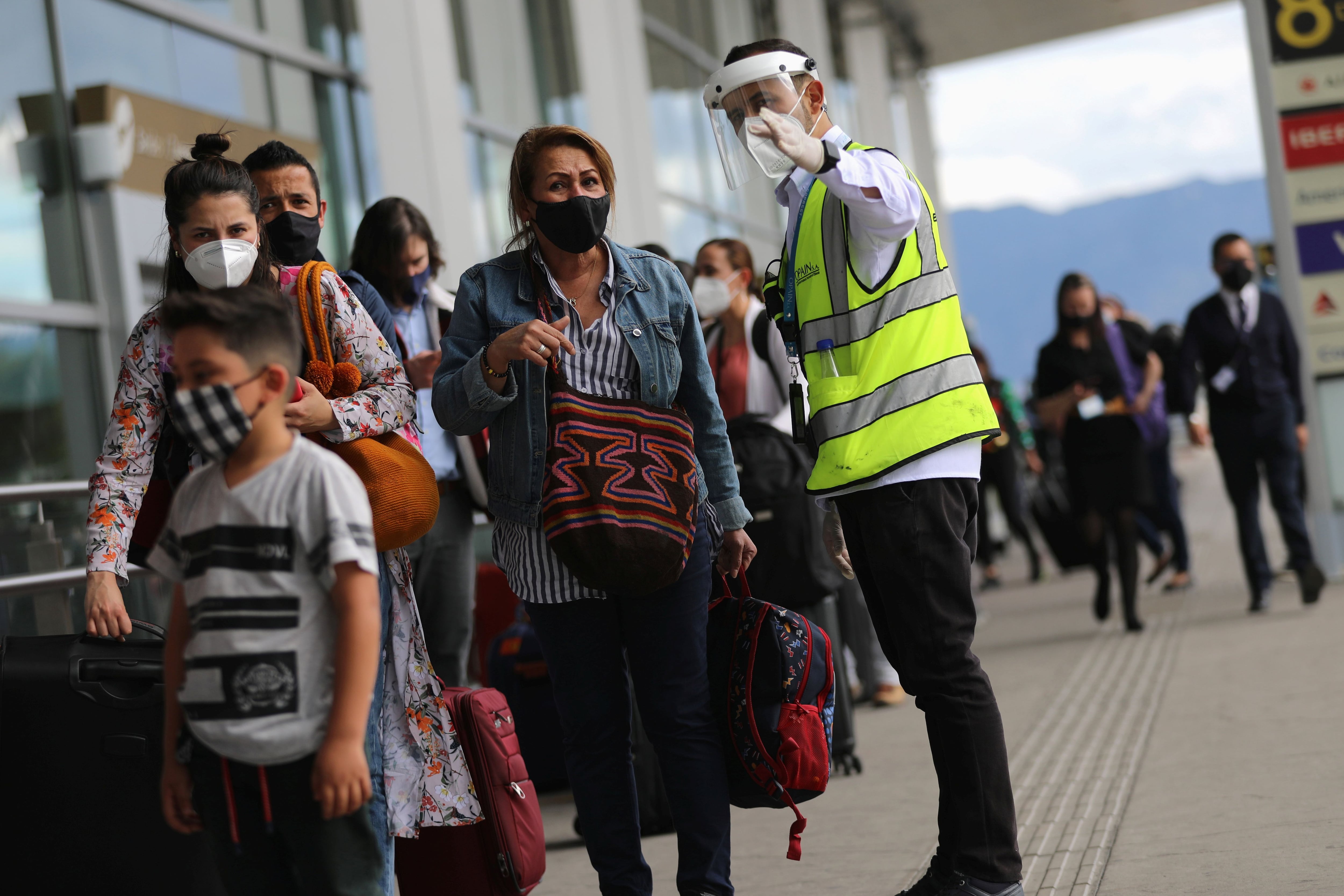 An employee of El Dorado International Airport wearing a face screen and mask gives directions to a female passenger, after the Colombian government decreed restrictions on flights from the United Kingdom, over fears of a new strain of the coronavirus, amid the spread of the coronavirus disease (COVID-19), in Bogota, Colombia December 21, 2020. REUTERS/Luisa Gonzalez