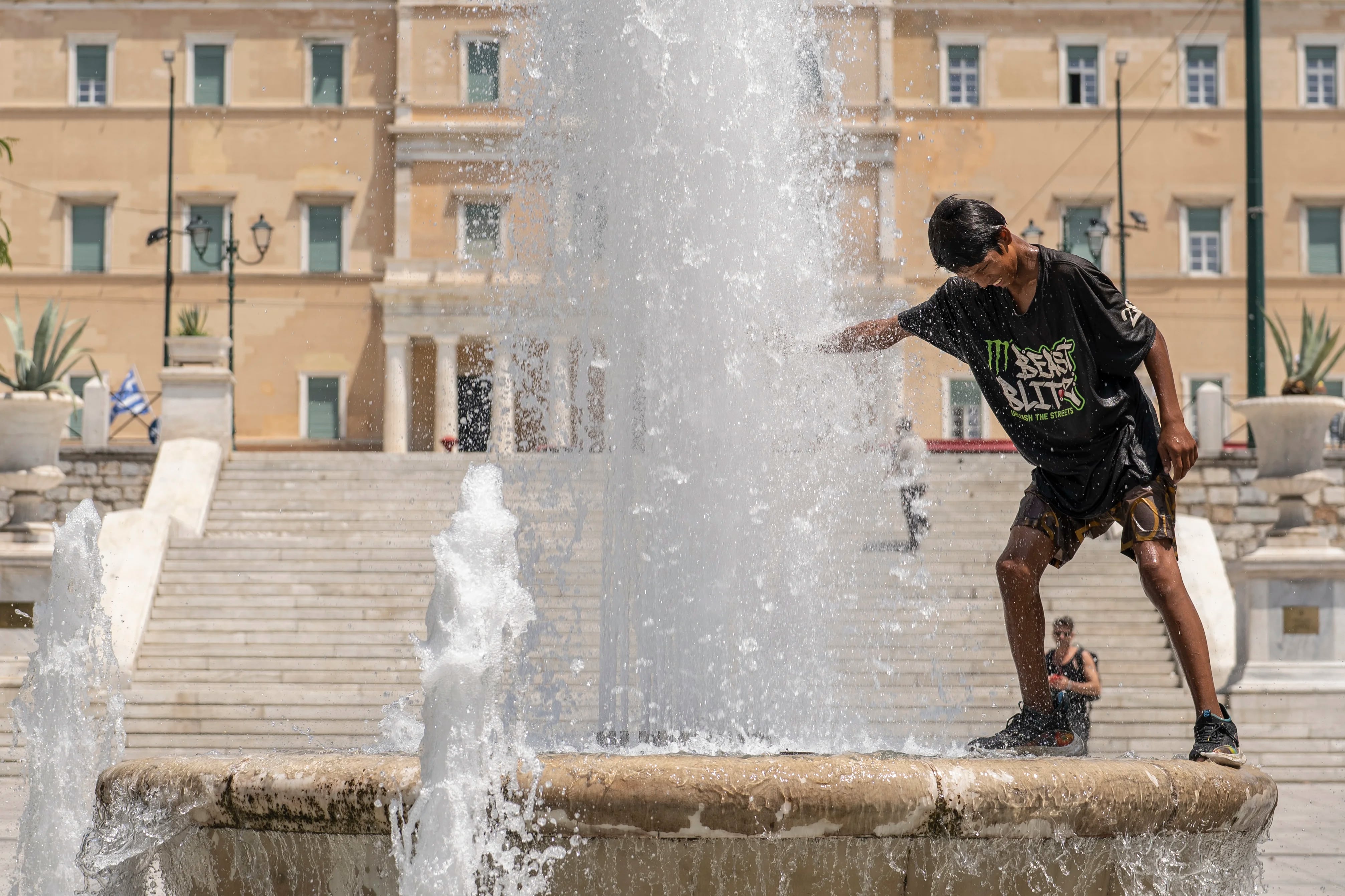Un joven se refresca con el agua de una fuente en Atenas, Grecia