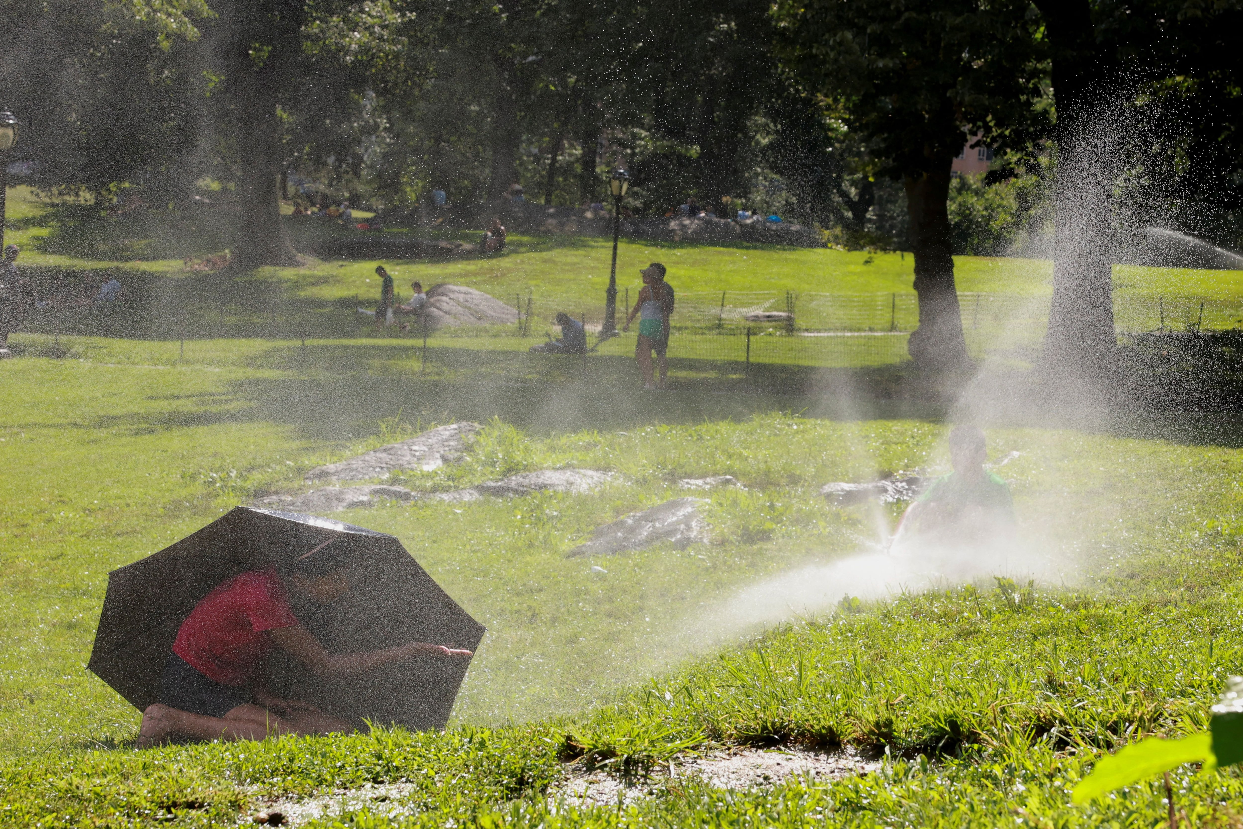 Un niño se refugia bajo un paraguas mientras otro juega con un aspersor de agua, en el Central Park de Manhattan, en Nueva York, Estados Unidos, 28 de julio de 2023. REUTERS/Amr Alfiky