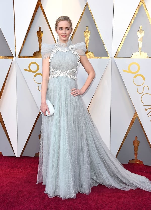 Emily Blunt en plumetí en gris hielo con mangas japonesas y cuello cisne. Lo acompañó con aros gota y clutch blanco para completar su look. El diseño está firmado por Schiaparelli