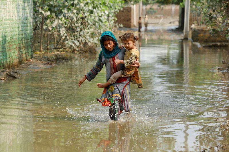 FOTO DE ARCHIVO. Una niña lleva a su hermano mientras camina entre el agua de las inundaciones en Pakistán (REUTERS/Fayaz Aziz)