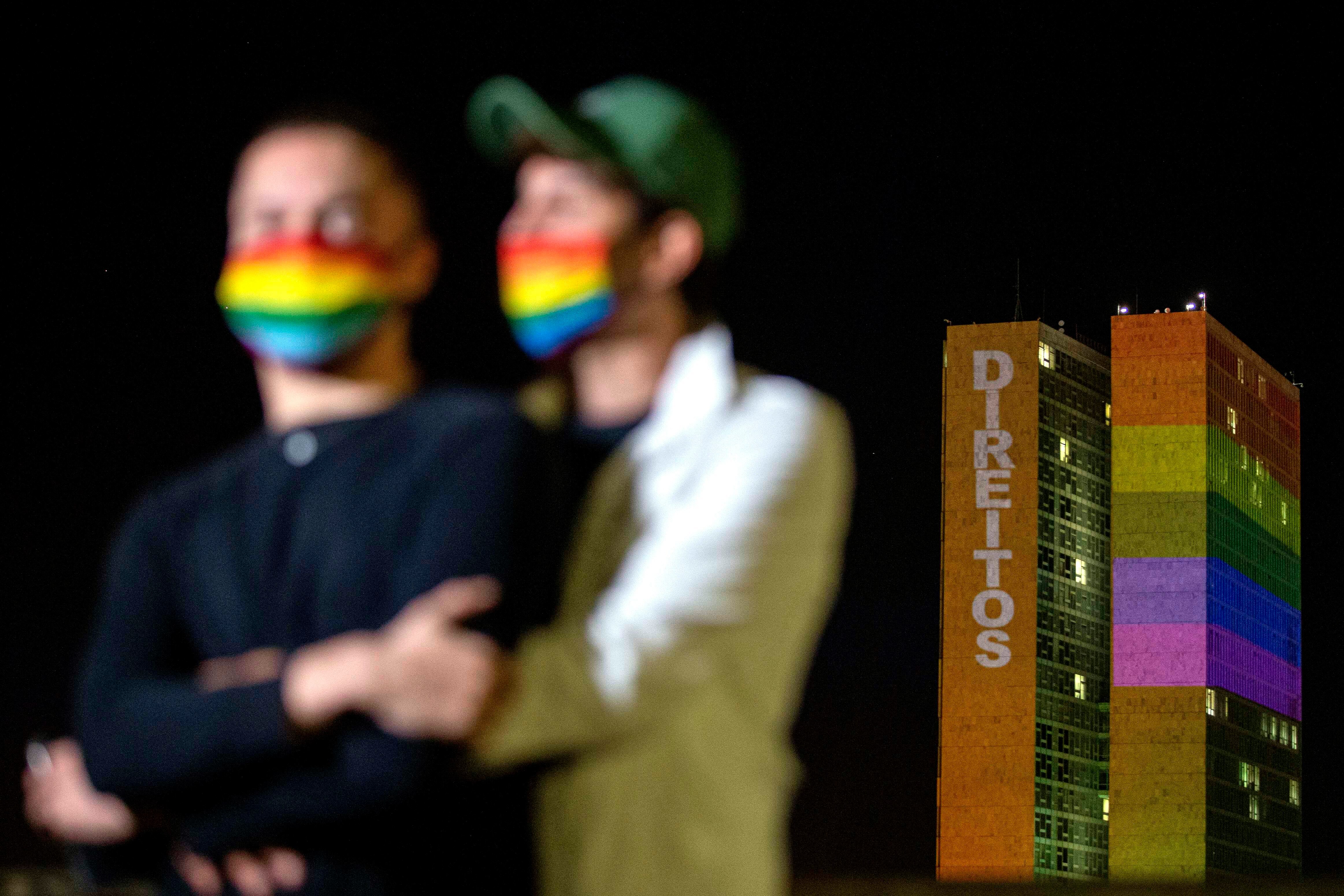 Los colores del arcoiris, la bandera del movimiento LGBTI, iluminaban la sede del Congreso Nacional de Brasil y proyectaban la palabra ""Derechos"" mientras una pareja protegida con mascarillas con los colores se abrazaban, en una conmemoración silenciosa y sin público del Día Internacional del Orgullo, en Brasilia (Brasil), el pasado 28 de junio. EFE/ Myke Sena/Archivo