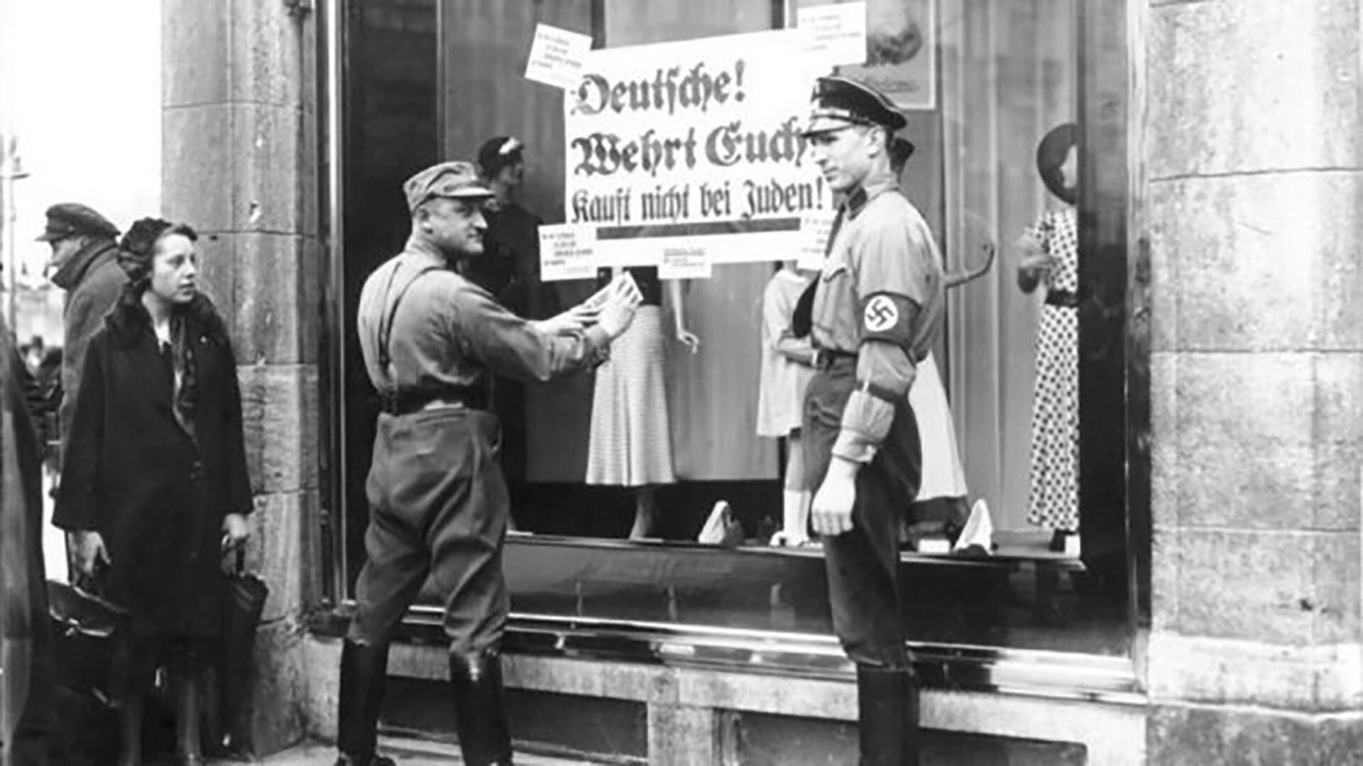 Miembros de las SS colocan una faja donde se indica que el dueño del negocio es judío. El 9 de noviembre de 1938 fueron destrozados más de siete mil comercios
