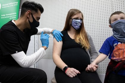 Aubrie Cusumano, embarazada de 39 semanas, recibe la vacuna de Pfizer-BioNTech contra la enfermedad del coronavirus (COVID-19) mientras sostiene la mano de su hijo Luca en la farmacia Skippack en Schwenksville, Pensilvania, Estados Unidos, el 11 de febrero de 2021.  REUTERS/Hannah Beier