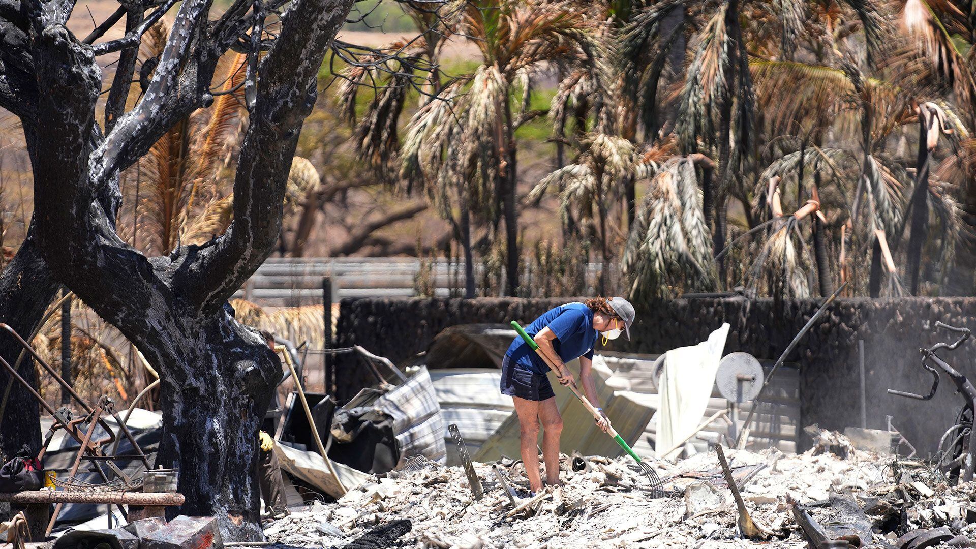 Una mujer remueve las cenizas entre los escombros de una casa destruida por un incendio forestal.