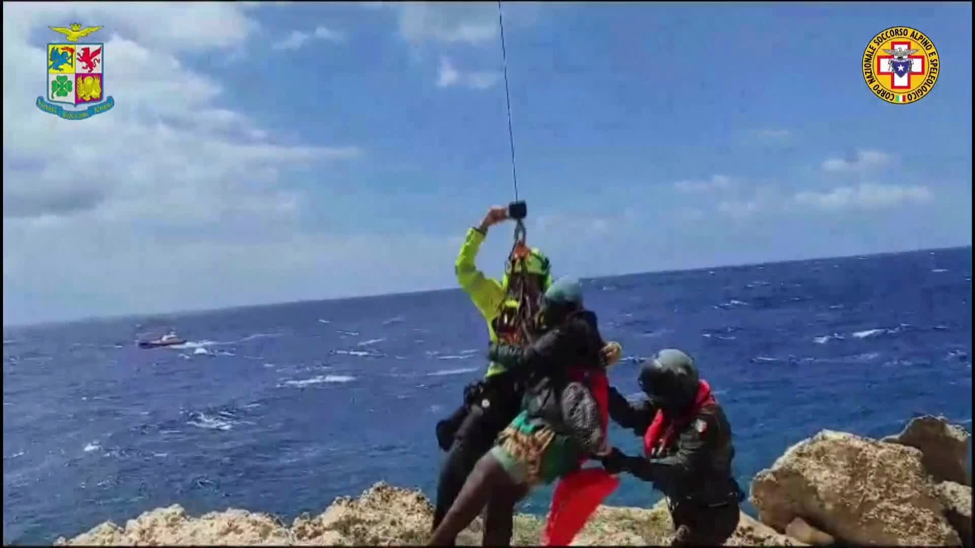 Un migrante varado en un arrecife rocoso en la diminuta isla de Lampedusa es ascendido a un helicóptero de rescate. (Rescate Alpino Italiano vía AP)