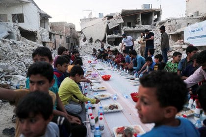 Niños comen su comida provista por un grupo de voluntarios en un vecindario dañado, Atarib, zona rural de Alepo, Siria.
REUTERS/Khalil Ashawi