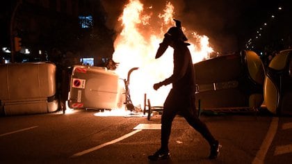 Un manifestante pasa junto a contenedores de basura en llamas durante los enfrentamientos con los Mossos d'Esquadra tras una protesta contra el encarcelamiento del rapero Pablo Hasél en Barcelona el 19 de febrero de 2021 (Foto de Pau BARRENA / AFP)