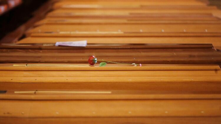 Una rosa roja yace sobre un ataúd alineado junto a otros dentro de la iglesia de San Giuseppe en Seriate, Italia, para ser bendecida antes de ser enviada a los crematorios en Udine y Venecia (AP)