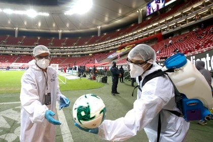 Personal del estadio Akron, de las Chivas del Guadalajara desinfectan el balón, previo al primer encuentro de la Liguilla de la Liga MX (Foto: AFP)
