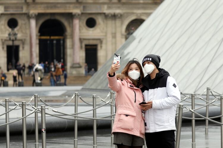 Una pareja se toma una selfie con barbijos delante del Museo del Louvre, en París - REUTERS/Charles Platiau