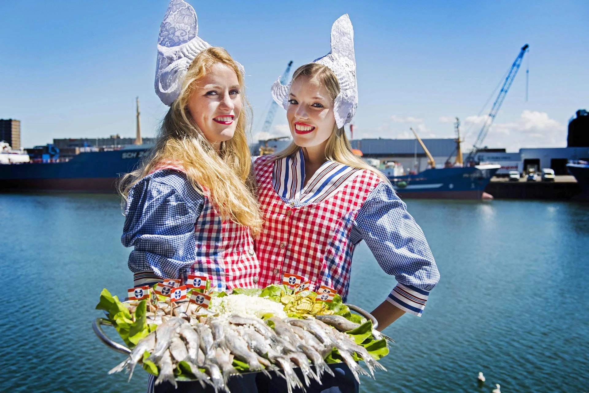 Dos mujeres vestidas al estilo tradicional de Holanda posan con arenques en el puerto de Scheveningen. El primer barril de arenques ha salido a subasta por 65.000 euros donados a caridad